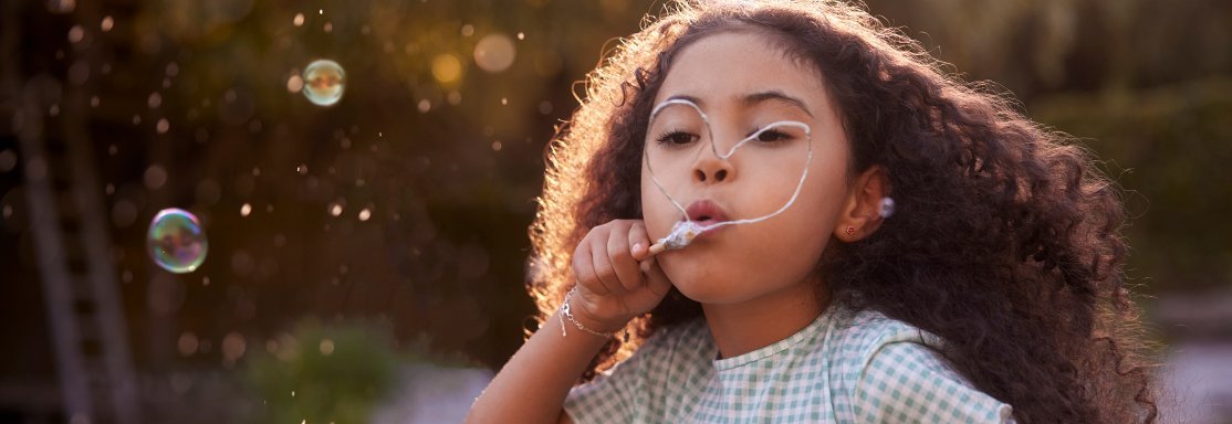 Fillette soufflant des bulles de savon en extérieur — image symbolisant l’enfance, l’espoir et la légèreté.