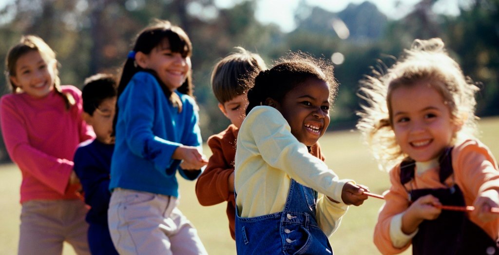 Enfants de différentes origines jouant au tir à la corde, souriants et unis dans une activité de plein air.