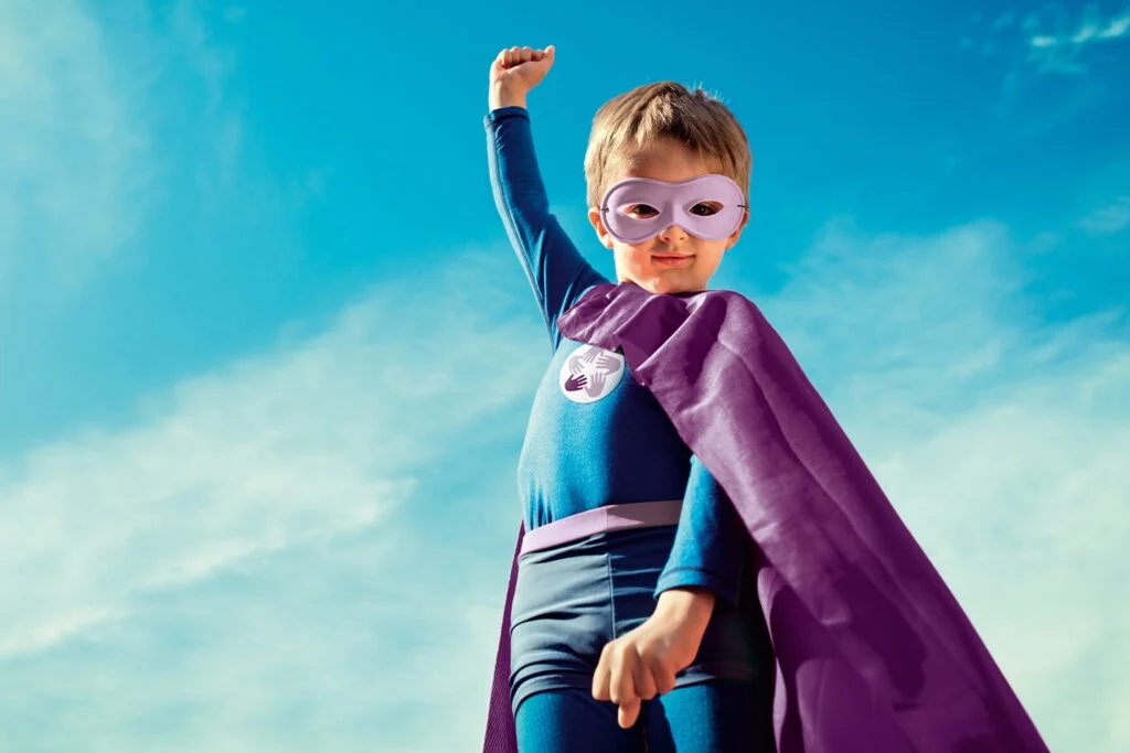 Enfant déguisé en super-héros levant le poing vers le ciel – symbole d’espoir, de force et d’autonomisation des jeunes.