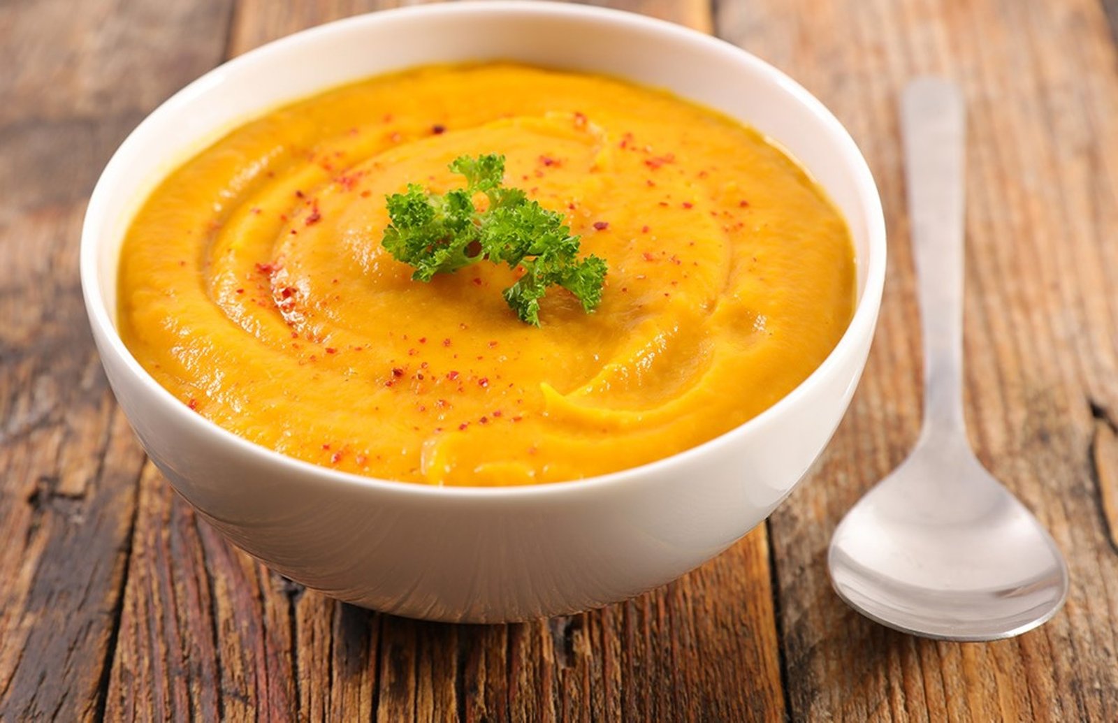 Bol de soupe orange onctueuse garni de persil et de piment sur table en bois