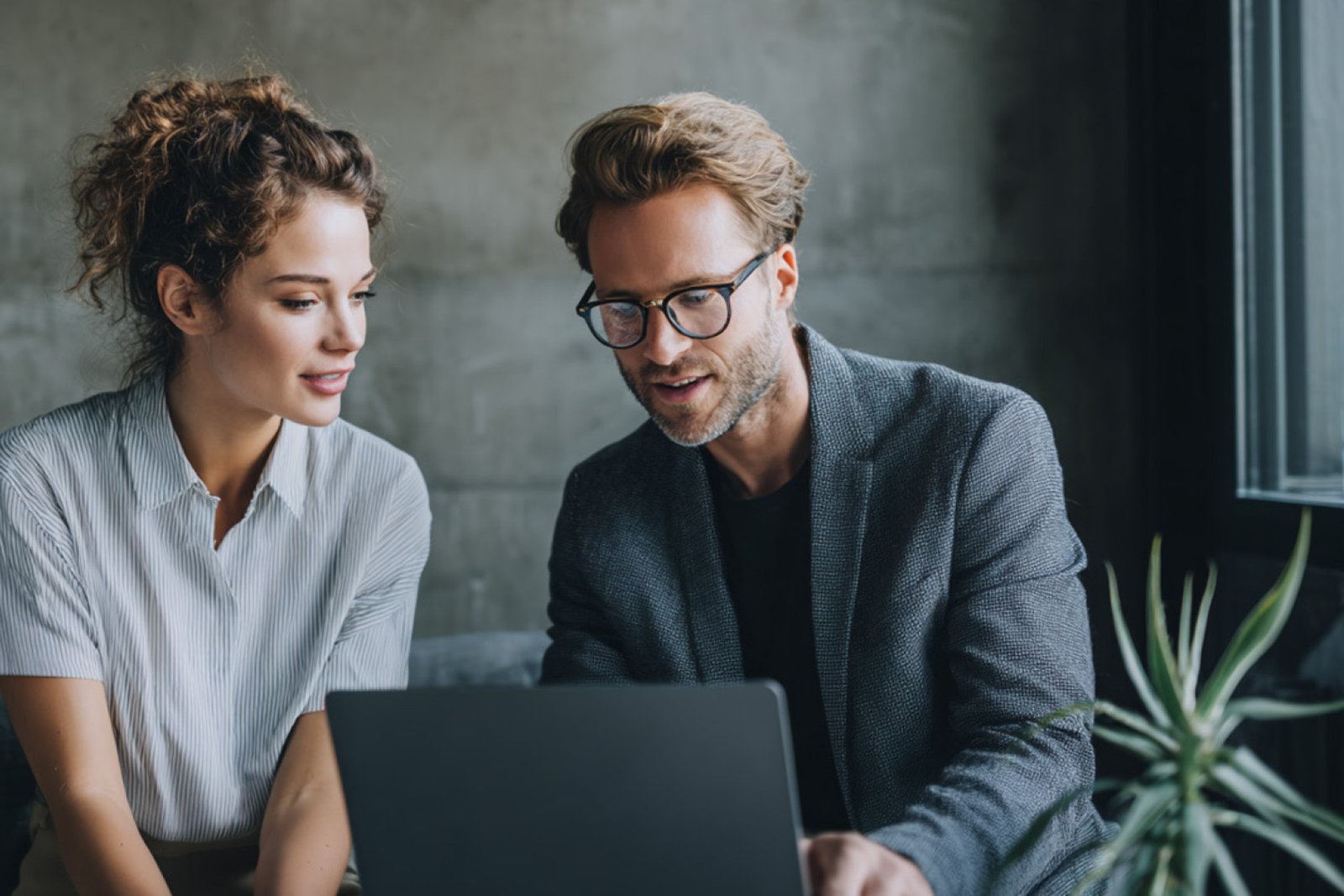 Deux personnes travaillent ensemble sur un ordinateur portable dans un bureau moderne. Elles regardent attentivement l'écran et discutent du contenu dans le cadre d'un environnement de travail collaboratif.